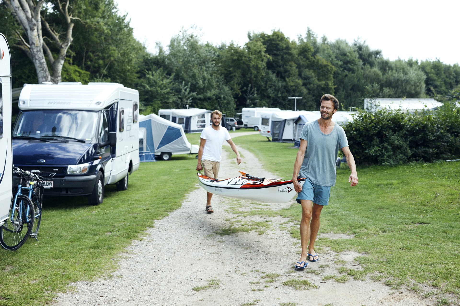 To personer bærer en båd gennem en campingplads