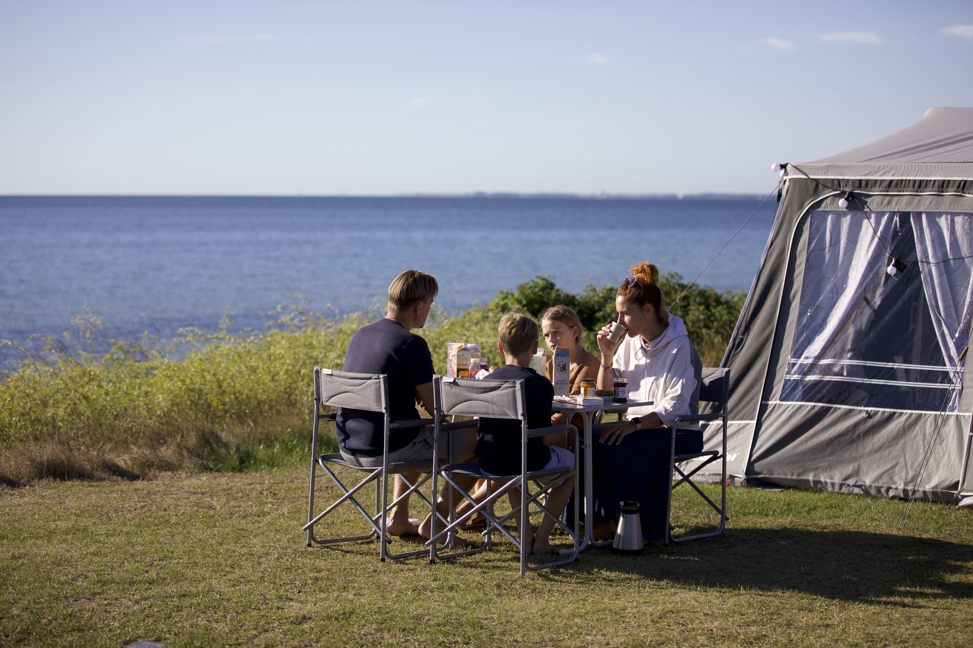 En familie spiser morgenmad på en campingplads med udsigt til vandet