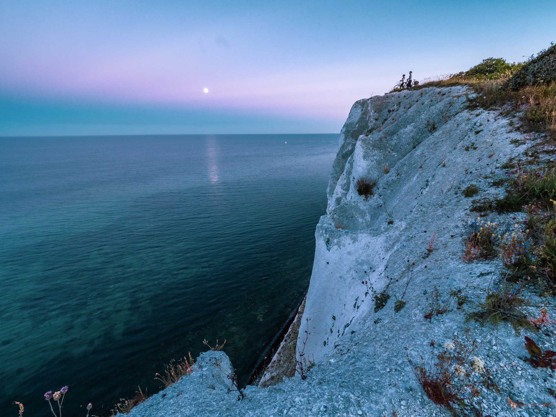 Foto af Møns Klint i solnedgang. To cyklister nyder udsigten på toppen af klinten. 