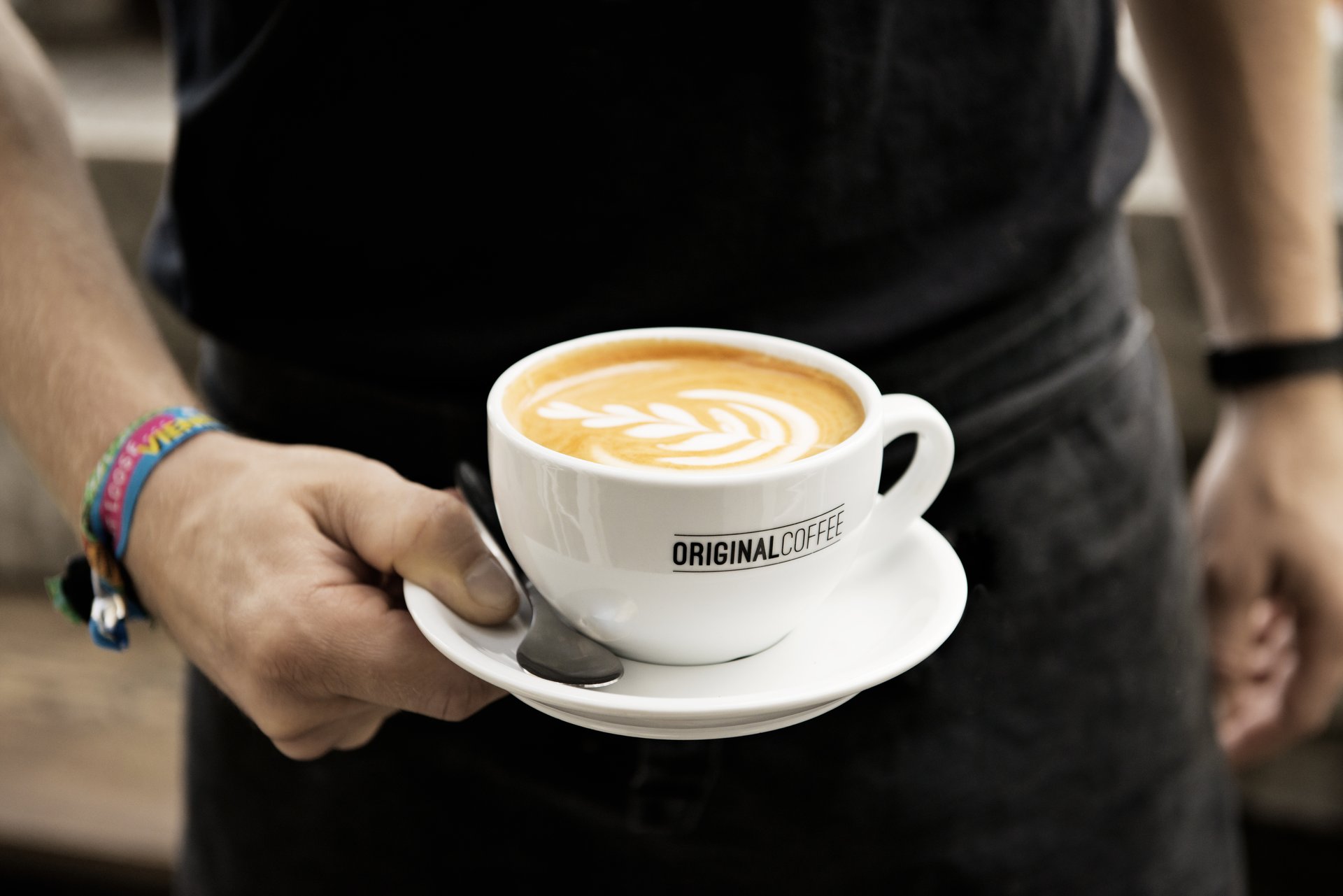 En hånd holder en friskbrygget kop kaffe fra Original Coffee