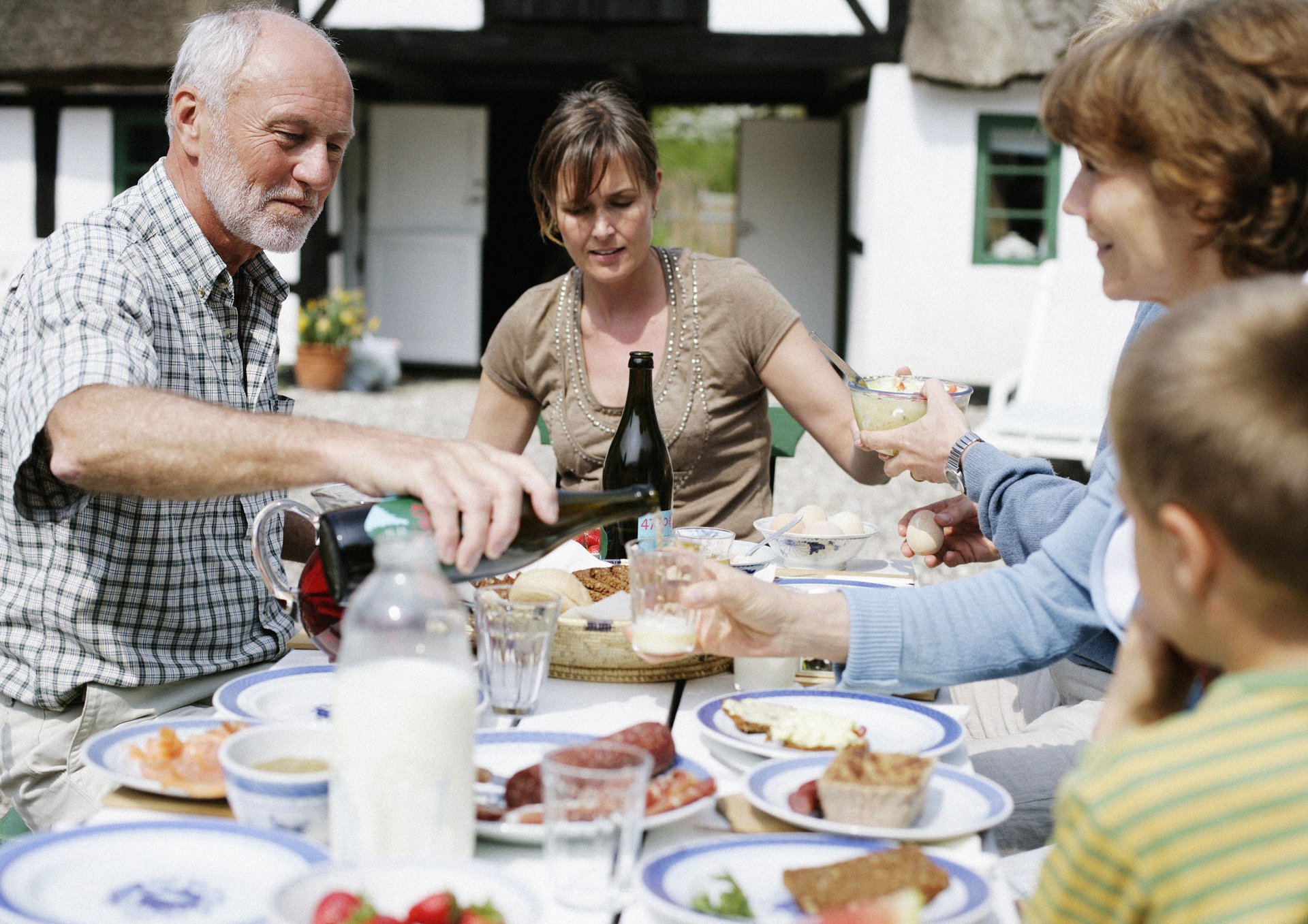 En familie spiser frokost udendørs ved en gård