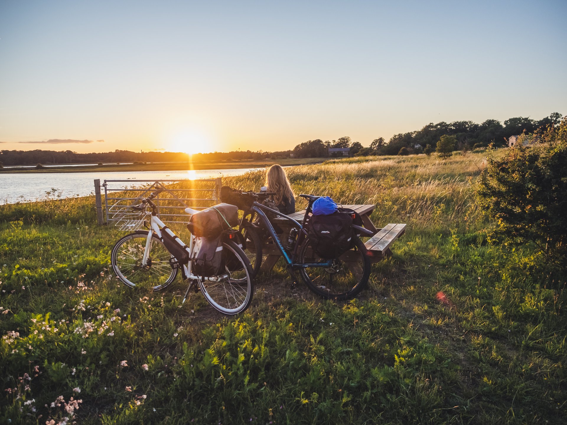 En person sidder i naturen på en bænk med sin cykle i solnedgangen
