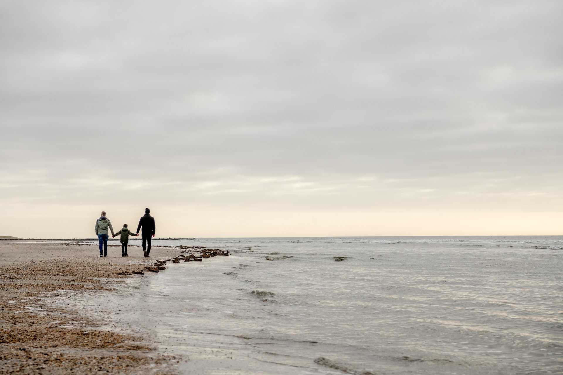 Tre personer går på stranden 